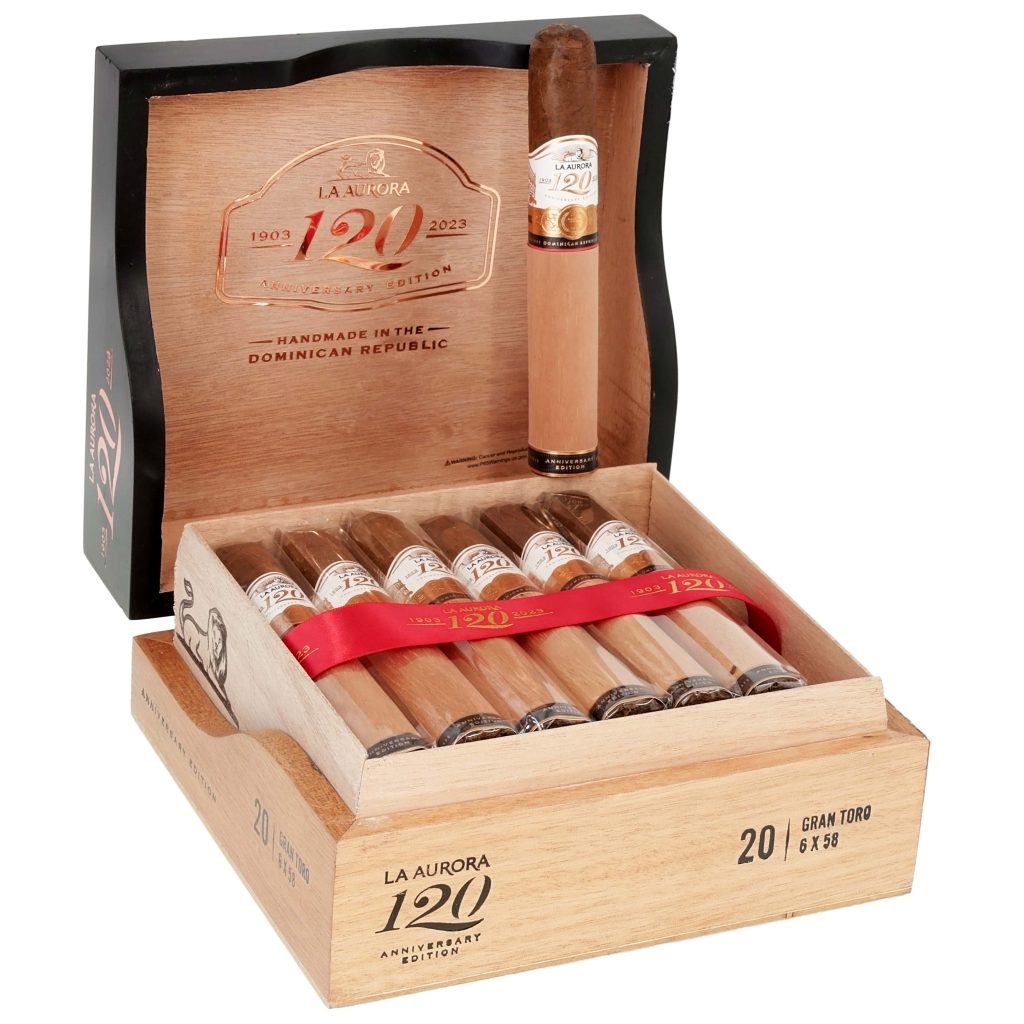 Wooden box of La Aurora 120 Anniversary Edition cigars showing Gran Toro vitolas with gold and red bands arranged inside cedar dividers, with one cigar standing against the open decorative lid.