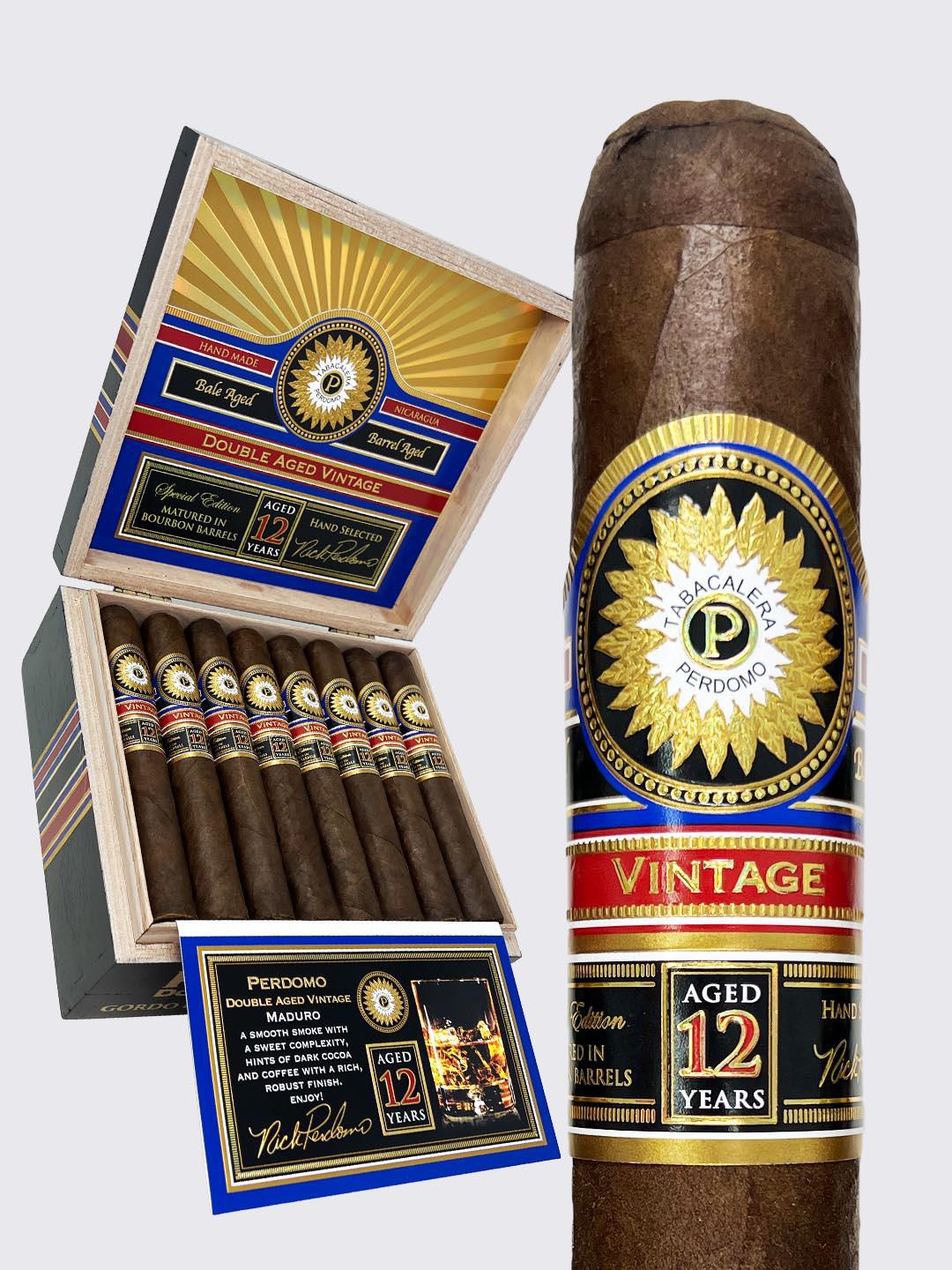 Perdomo Double Aged 12 Year Vintage Maduro Robusto cigar displayed next to its wooden box featuring ornate blue, red, and gold banding with 'AGED 12 YEARS' prominently displayed